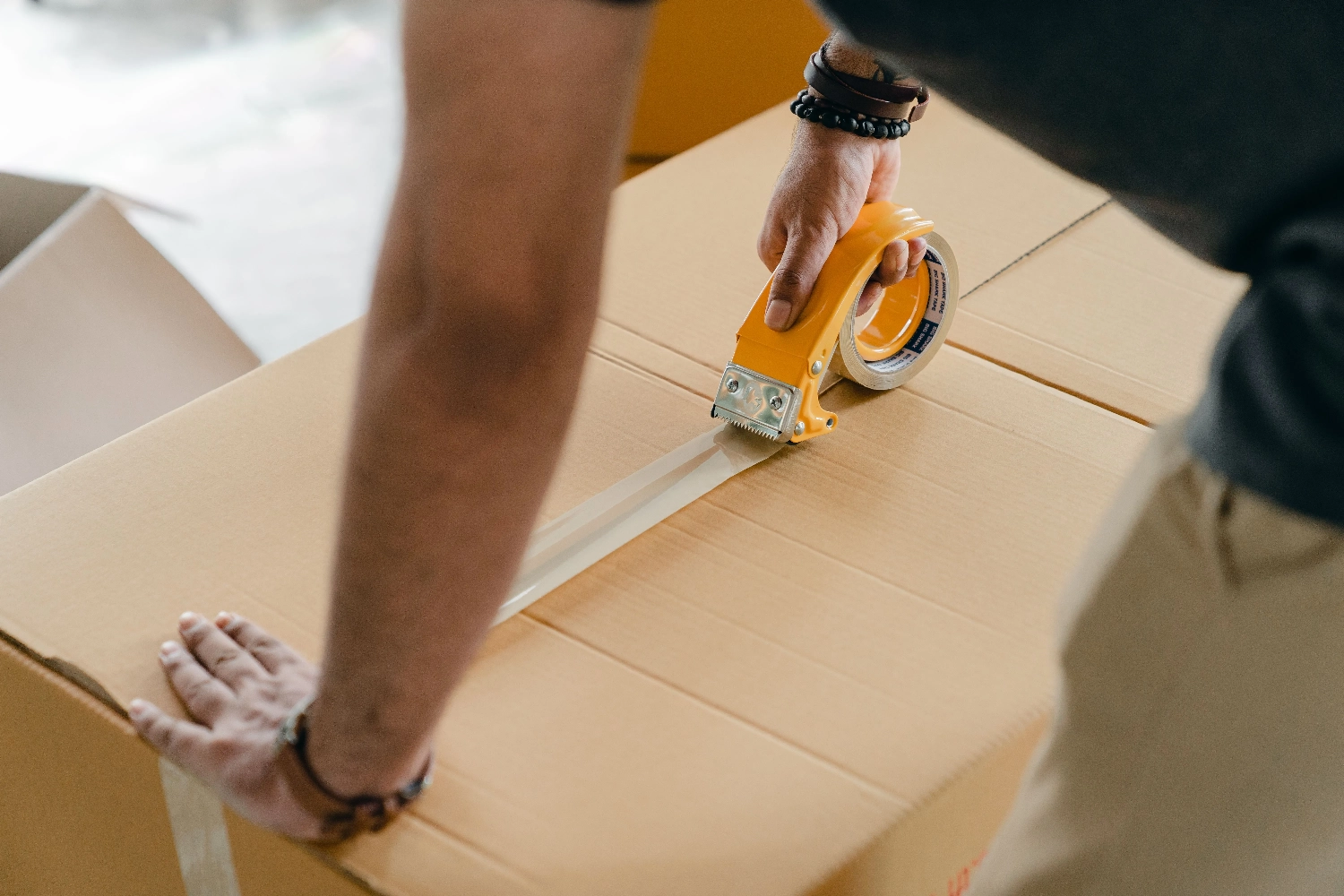 Jova – Logistikdienstleistungen – Packbandabroller: Ein gelbes Handgerät zum effizienten Aufbringen von Klebeband auf Kartons.